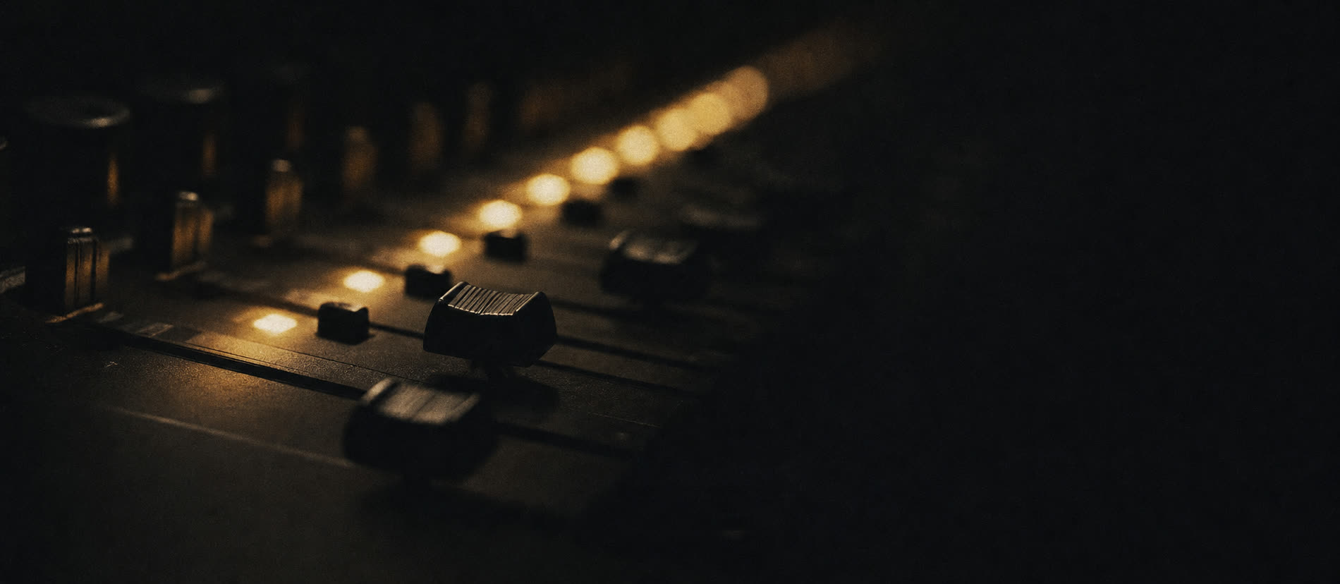 Detail of a mixing console channel strip lit by a single row of warm indicator lights.